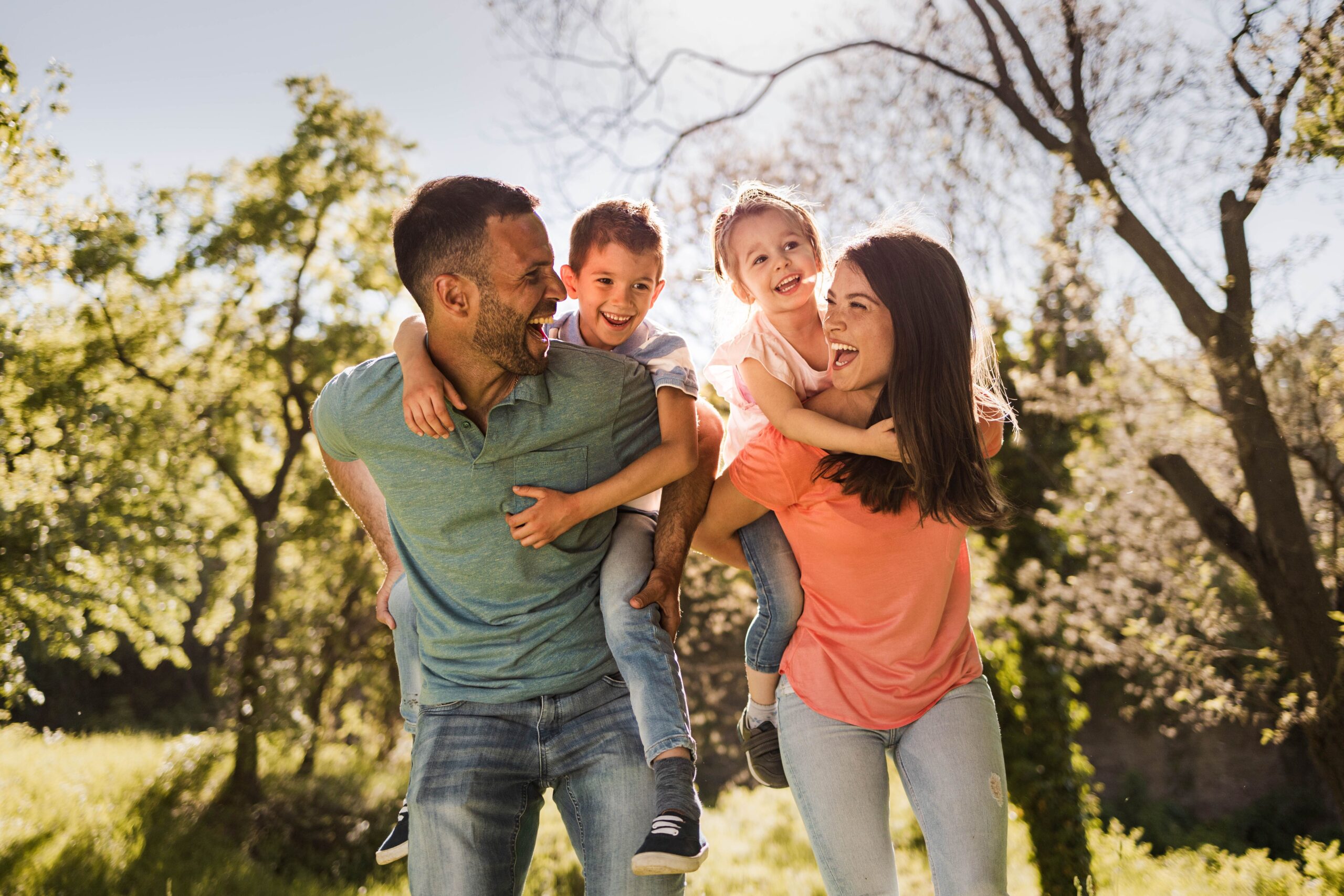 Happy parents having fun while piggybacking their small kids in nature.